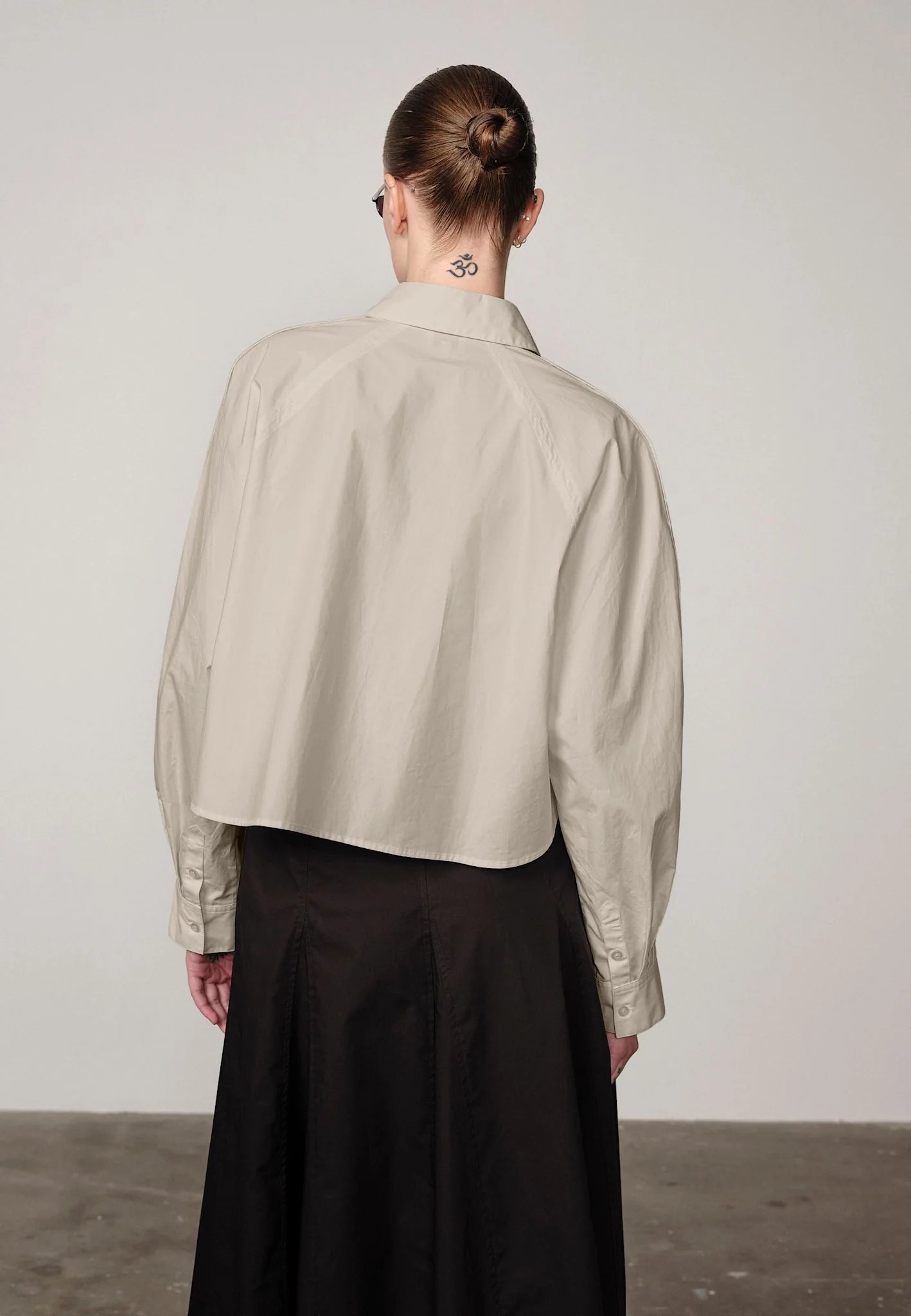 Woman wearing an oyster white Elsie shirt by Herskind and black skirt against a plain background