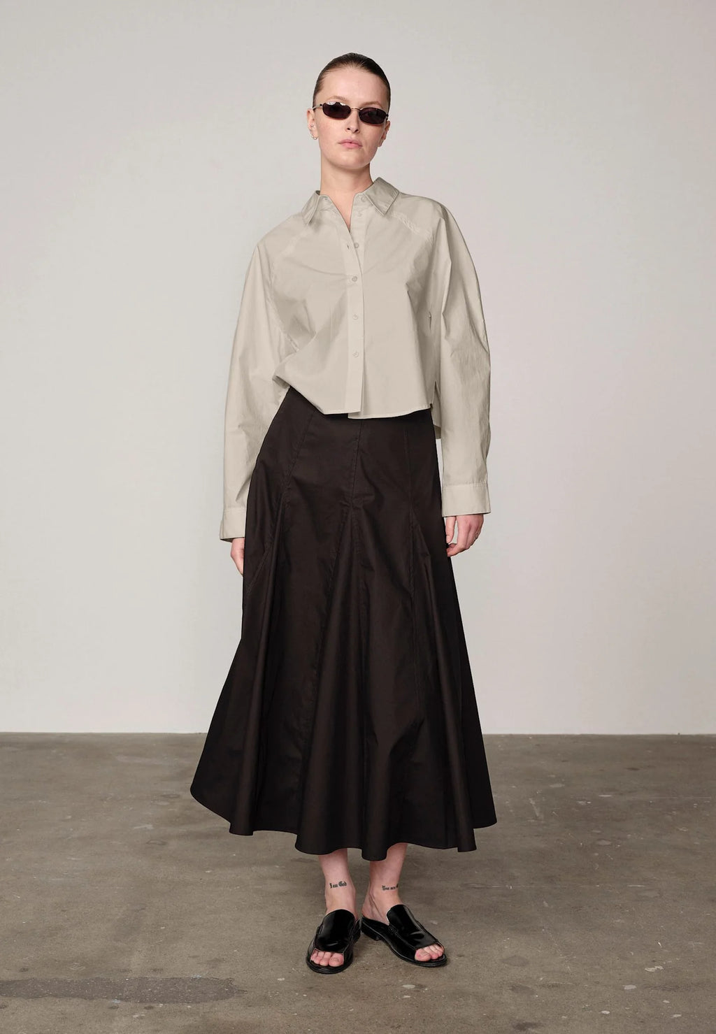 Woman wearing an oyster white Elsie shirt by Herskind and black skirt against a plain background