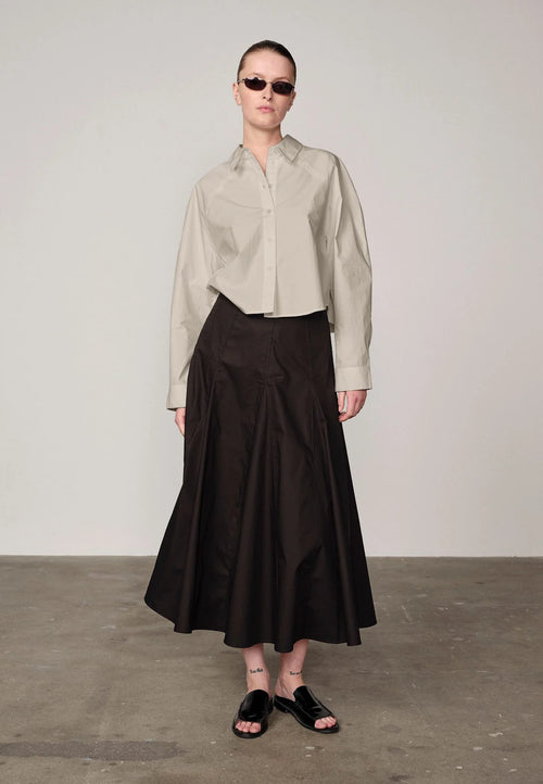 Woman wearing an oyster white Elsie shirt by Herskind and black skirt against a plain background
