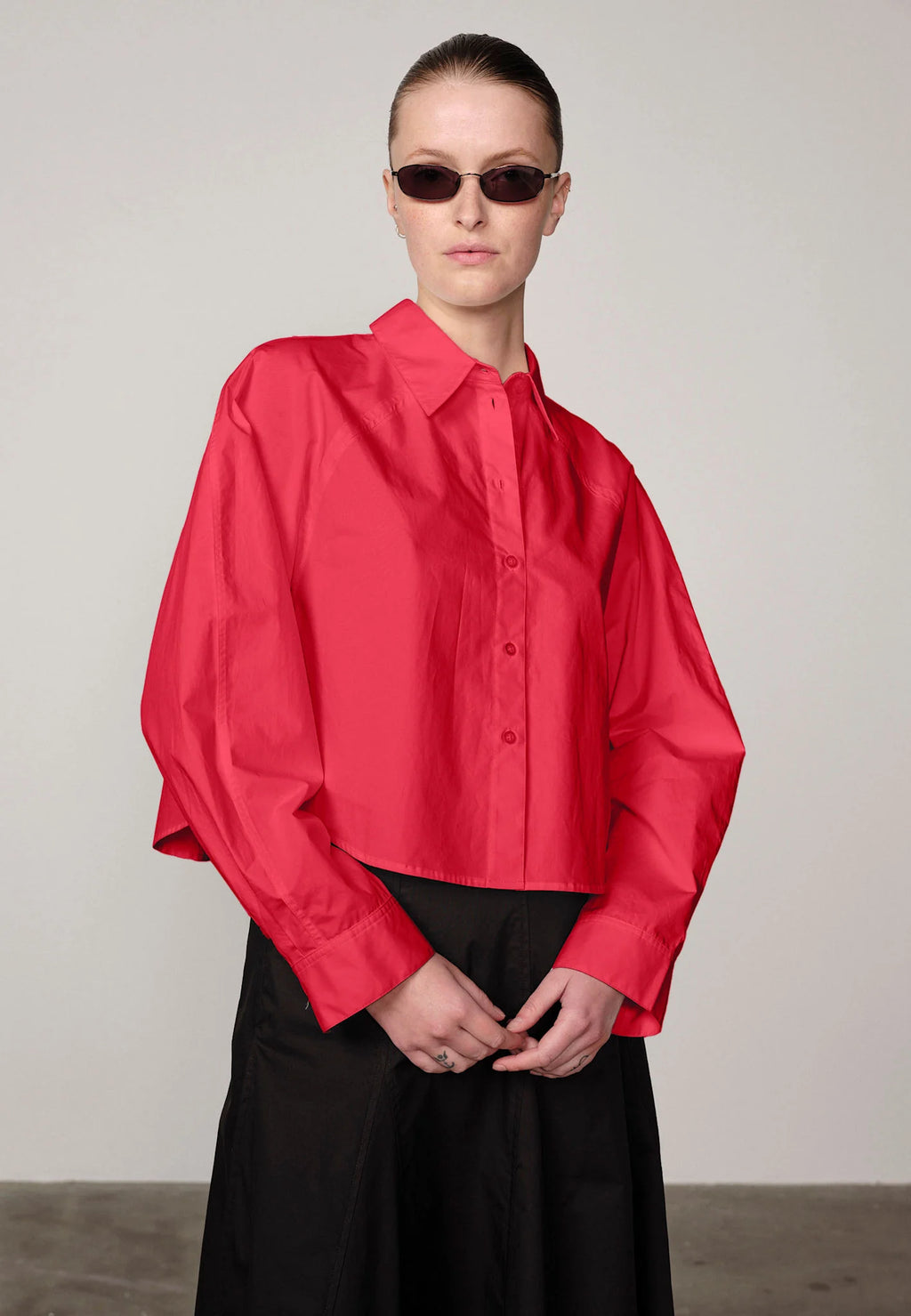 Woman wearing a red Elsie shirt by Herskind and black skirt against a plain background