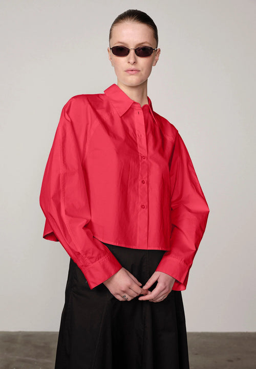 Woman wearing a red Elsie shirt by Herskind and black skirt against a plain background