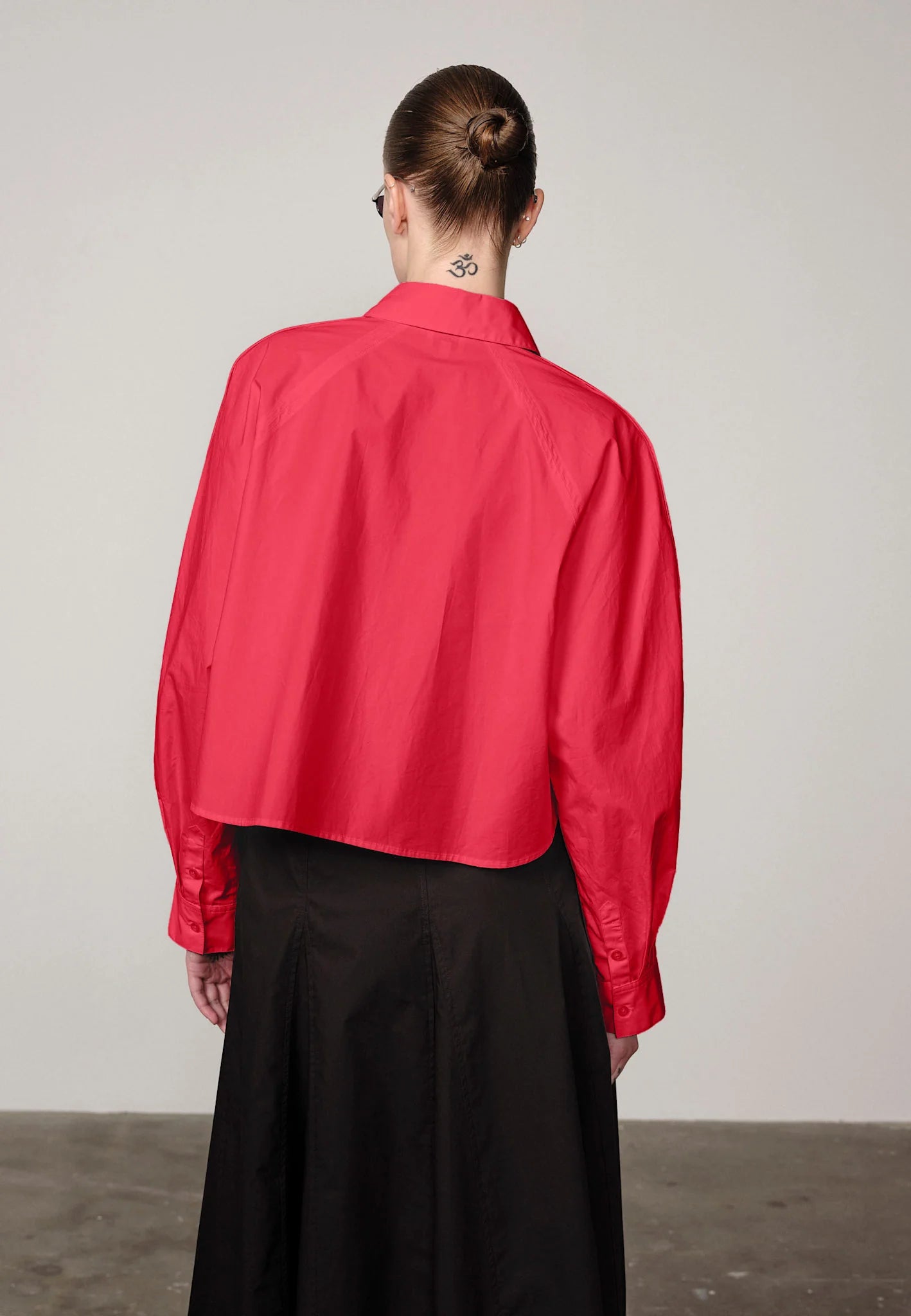 Woman wearing a red Elsie shirt by Herskind and black skirt against a plain background