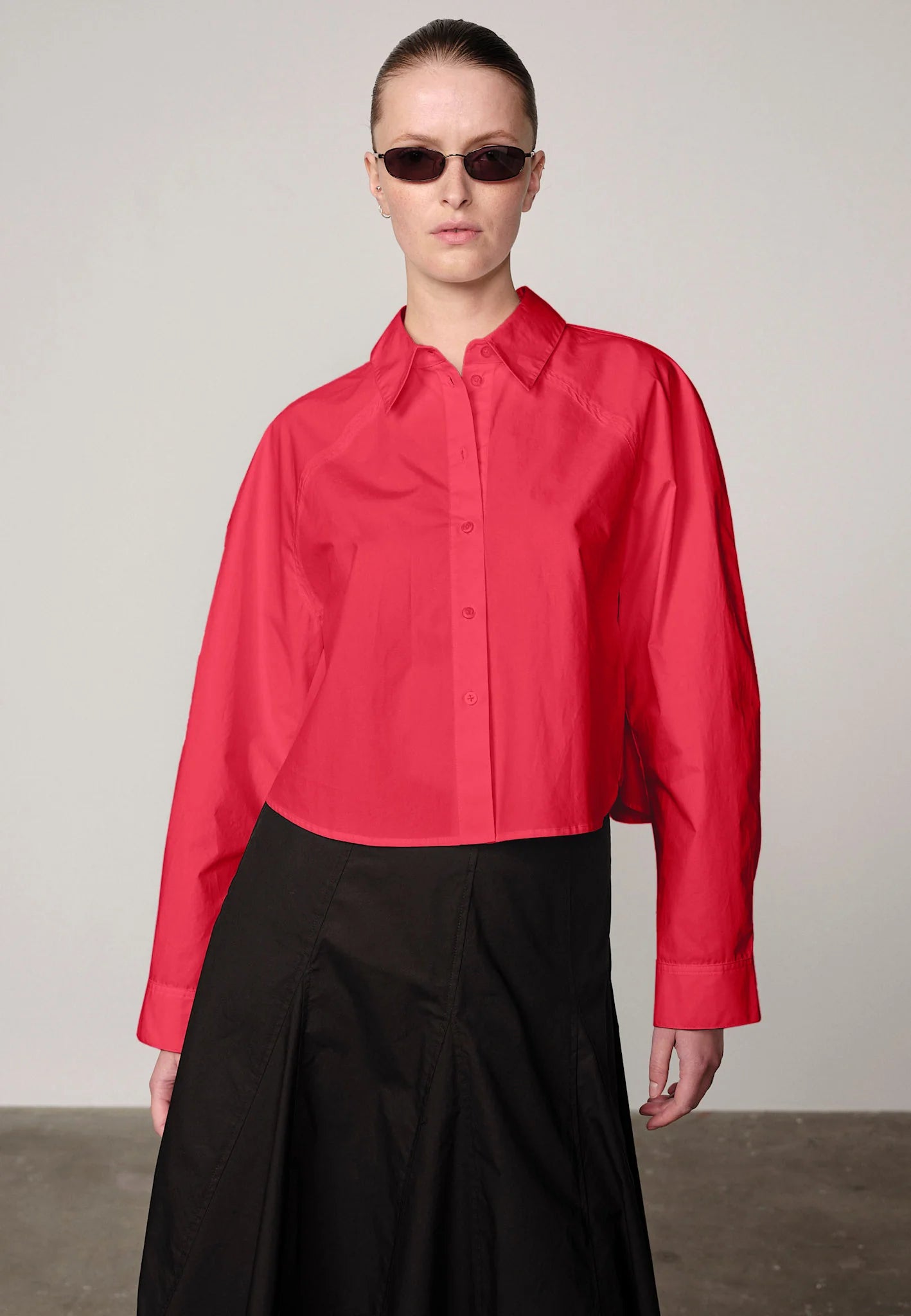 Woman wearing a red Elsie shirt by Herskind and black skirt against a plain background