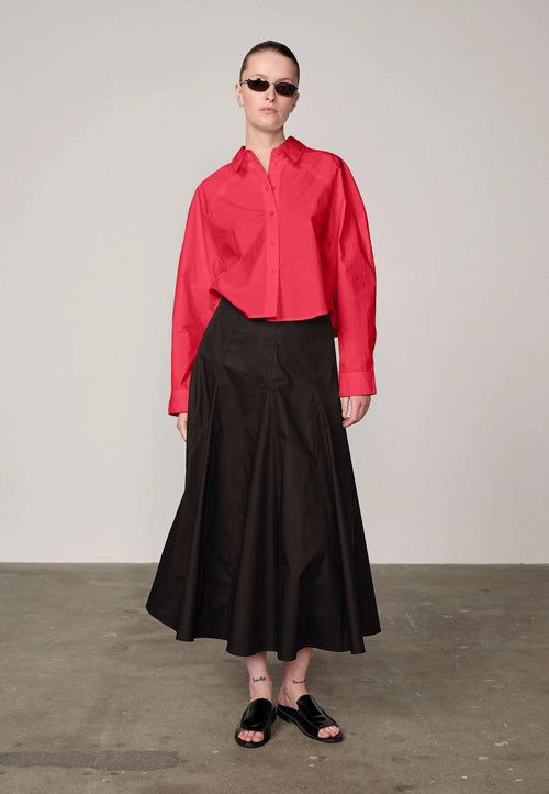 Woman wearing a red Elsie shirt by Herskind and black skirt against a plain background