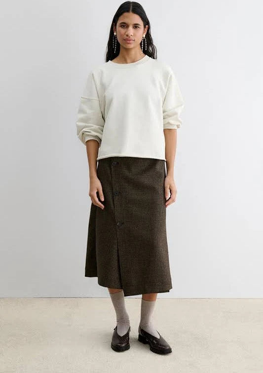 A a woman wearing a pair of dark brown clog-style slingback Lenox Lug shoes by Rachel Comey with an embossed crocodile pattern, black platform soles, and adjustable ankle straps, shown against a light gray background.