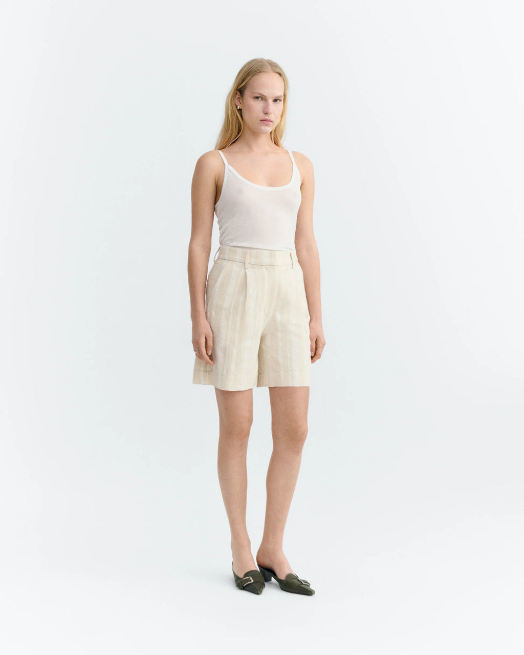 Woman wearing a white tank top and raw beige with white stripes shorts on a white background