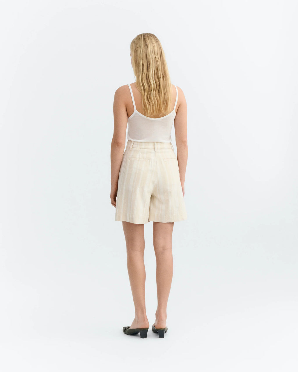 Woman wearing a white tank top and raw beige white stripes shorts on a light white background