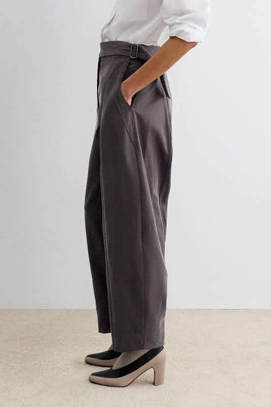 A person wearing dark charcoal gray barrel-leg midnight pants by Rachel Comey, styled with a white shirt and black-and-beige heels, shown from the waist down against a neutral studio background.