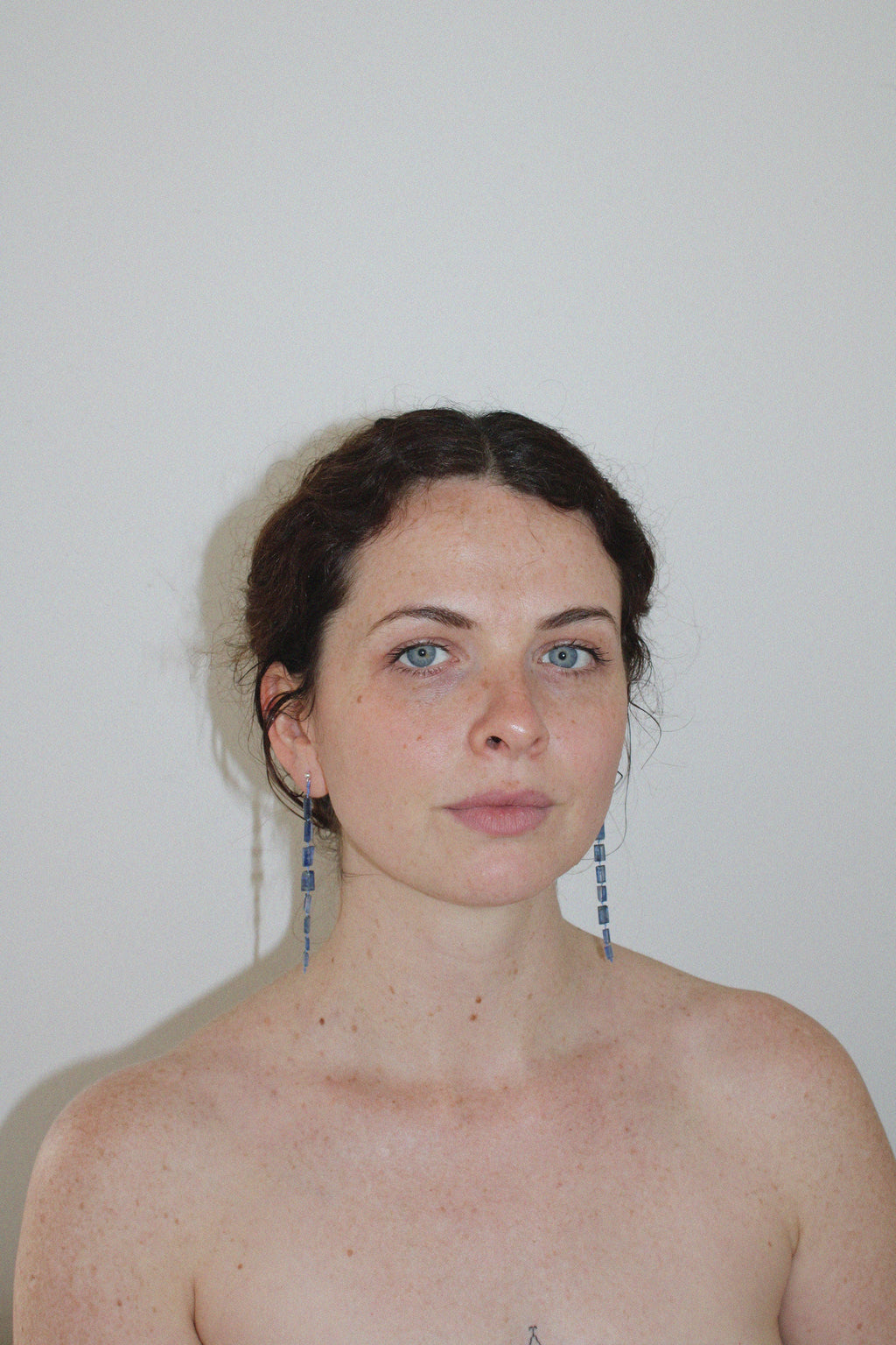 Woman with blue drop midnight earrings against a plain background