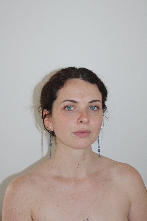 Woman with blue drop midnight earrings against a plain background
