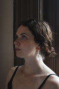 A woman in profile wearing a clear, teardrop-shaped dangle moonlight earring by Takara, photographed in warm, dim indoor light.