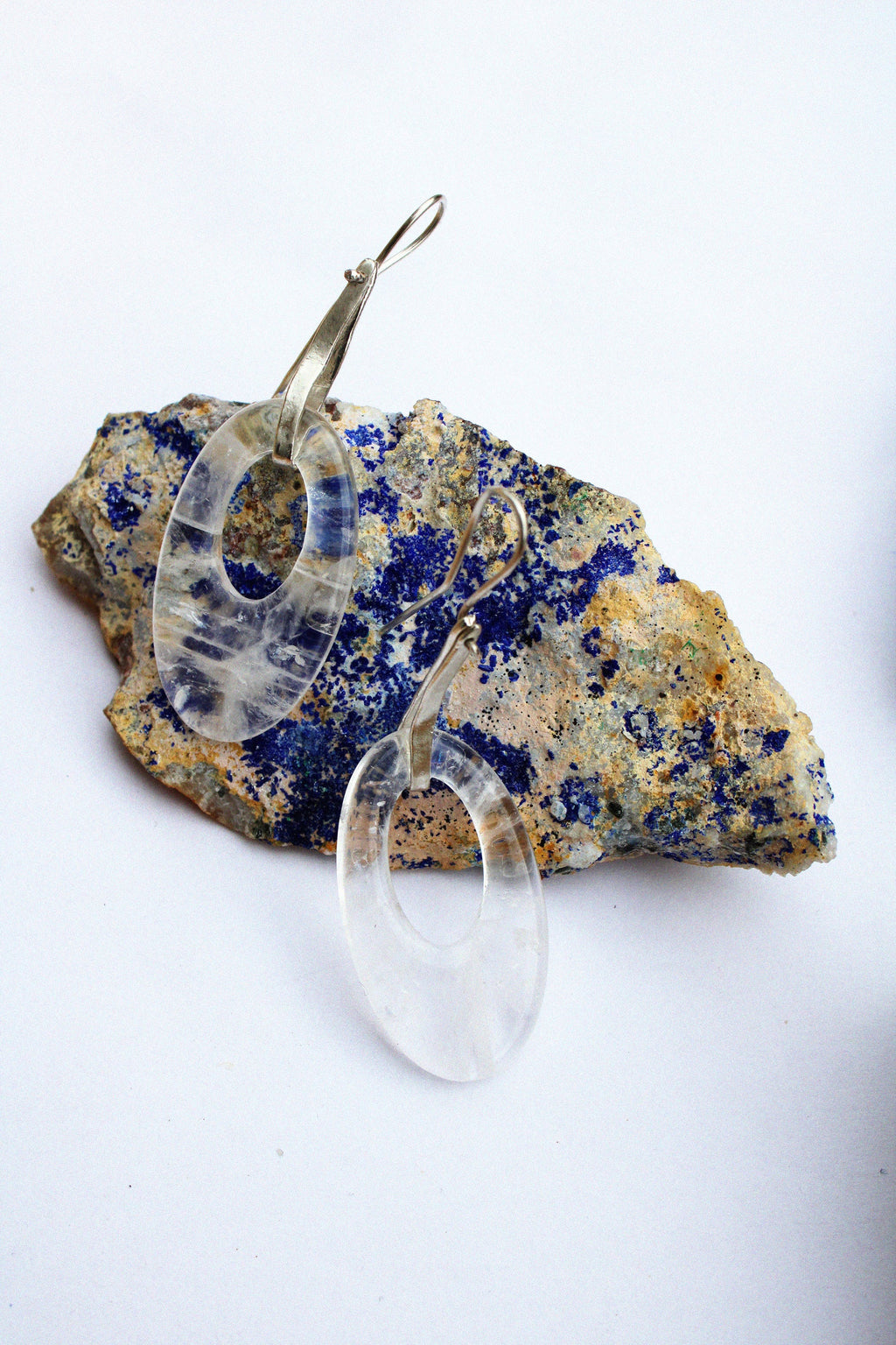 A clear, teardrop-shaped dangle moonlight earring by Takara, on a colorful stone.