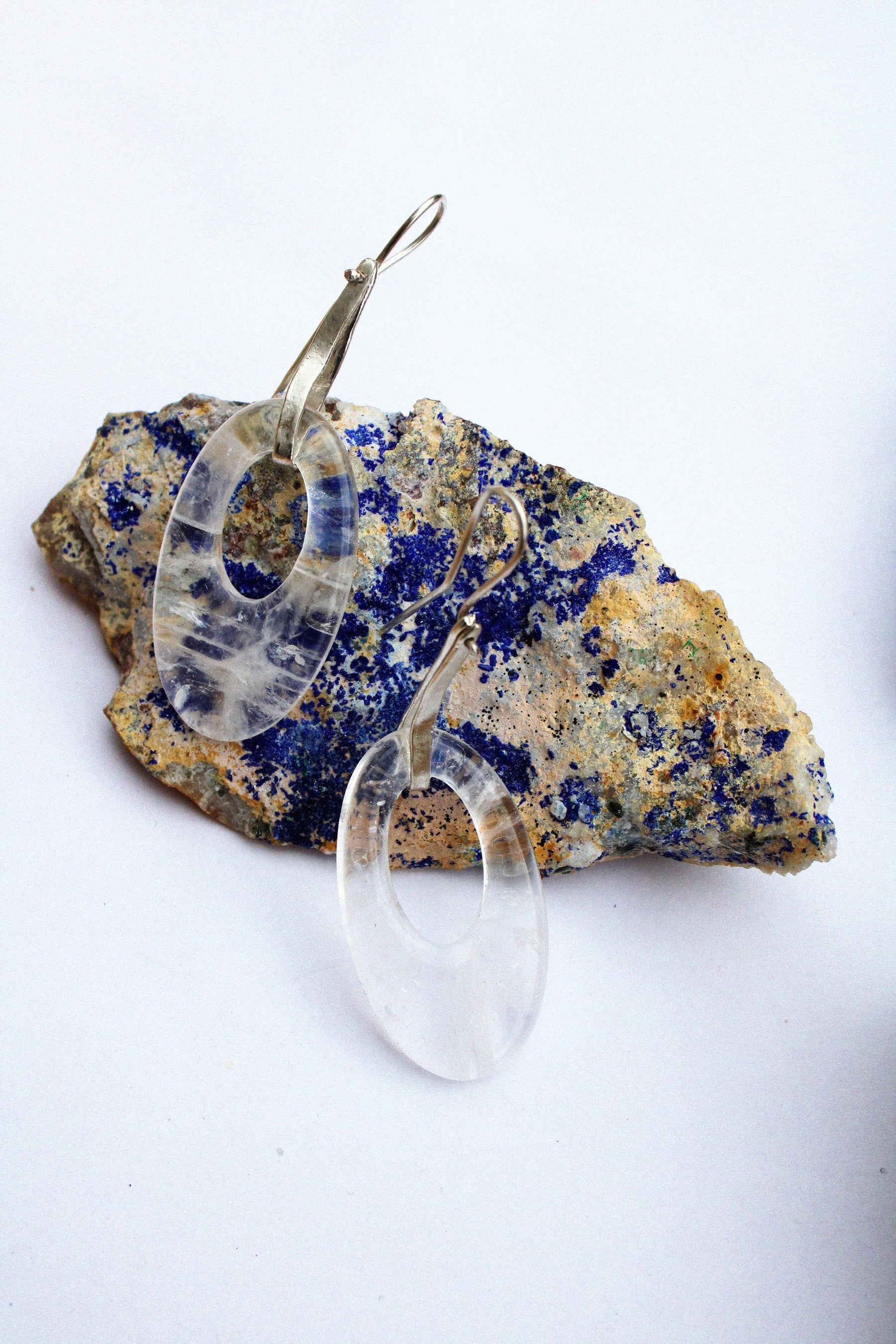 A clear, teardrop-shaped dangle moonlight earring by Takara, on a colorful stone.