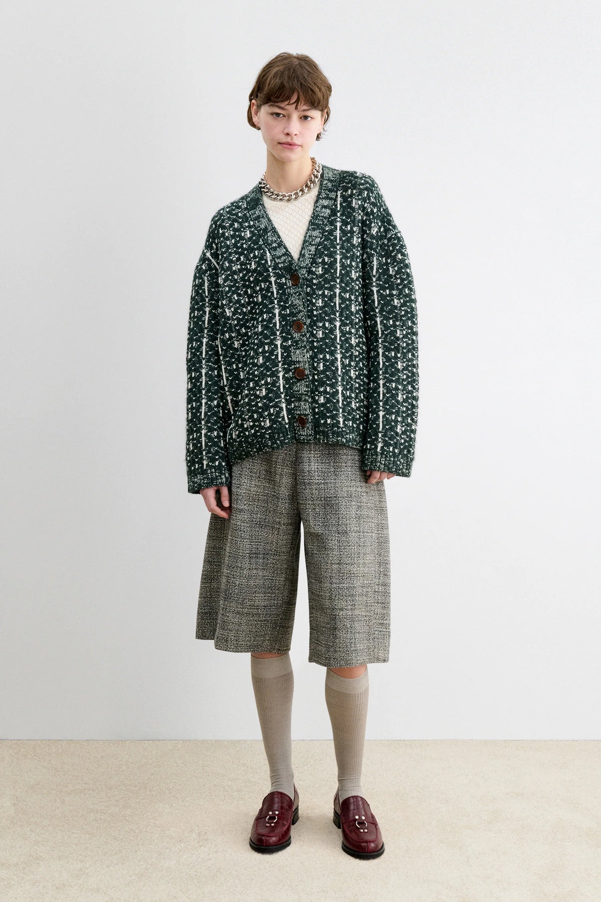 A Model wearing a forest fair isle knit Hedda Cardigan by Rachel Comey with grey shorts.