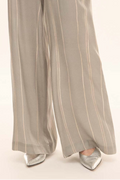 Close-up of a person wearing wide-leg taupe pants with thin vertical cream stripes and metallic silver pointed-toe flats, shown from the knees down against a plain light background.