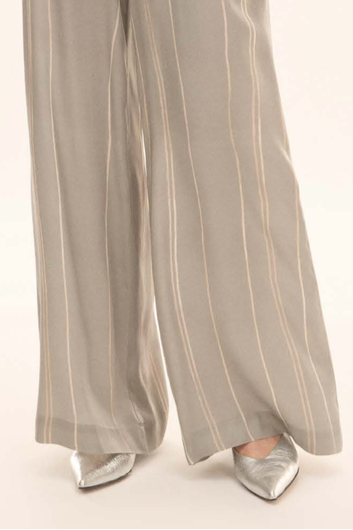 Close-up of a person wearing wide-leg taupe pants with thin vertical cream stripes and metallic silver pointed-toe flats, shown from the knees down against a plain light background.