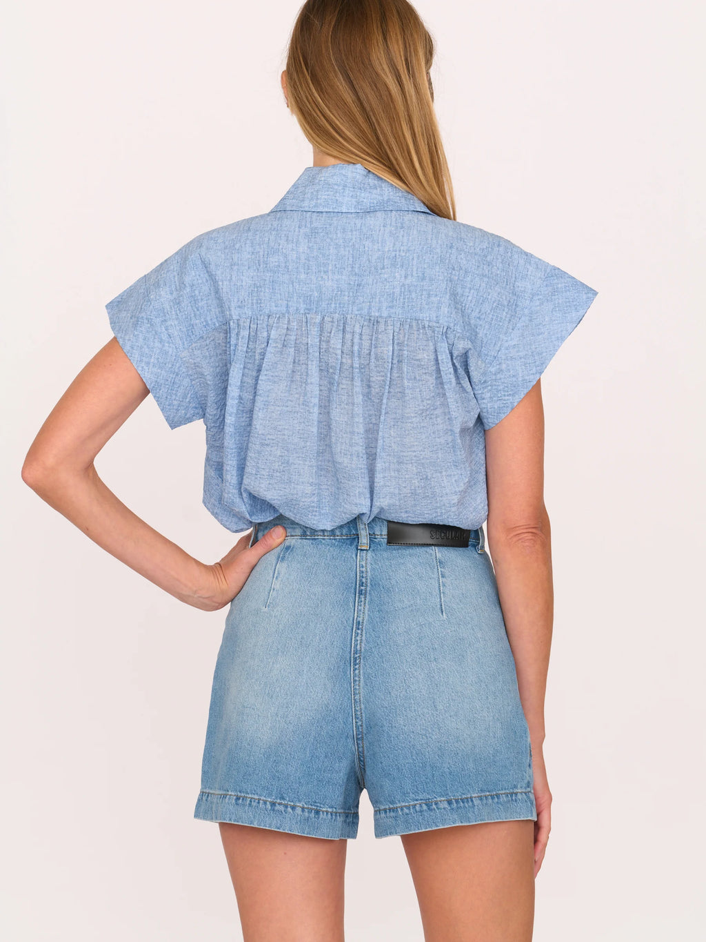 Woman wearing a light blue top and Secular denim shorts on a white background