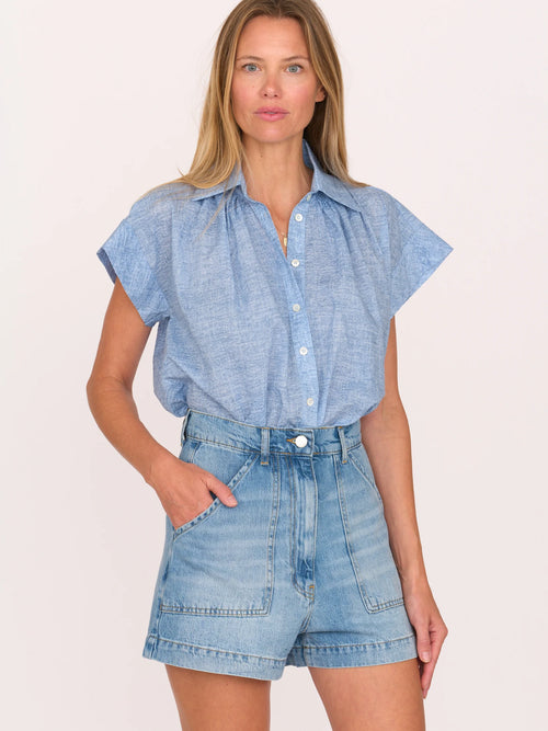Woman wearing a blue shirt and denim shorts by Secular on a white background