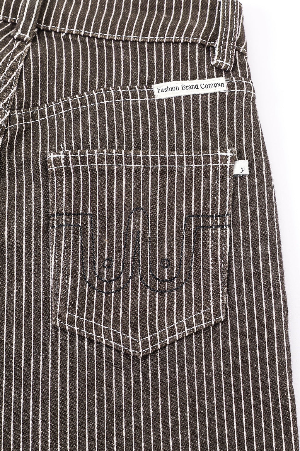 Close-up of the back pocket of dark brown pinstriped jeans with white vertical stripes, featuring black embroidered stylized boobs and a white brand label. Thin Railroad stripe jeans by Fashion Brand Company.