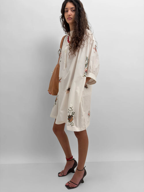 Woman wearing a white dress with floral print against a plain background