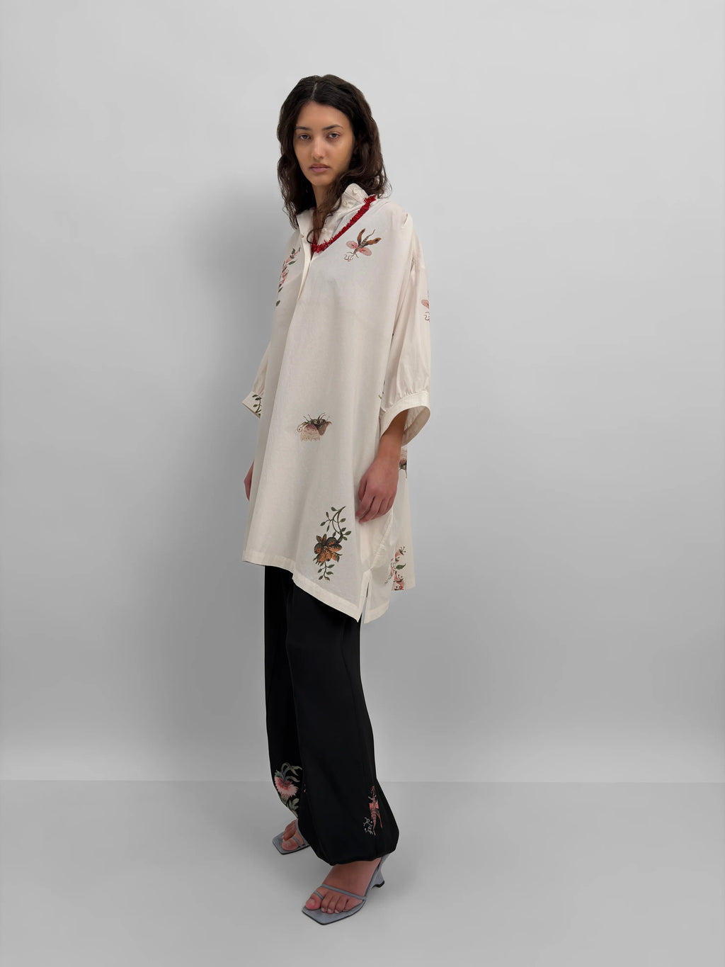 Woman wearing a cream-colored floral dress with black pants on a gray background