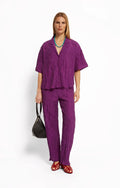 Woman wearing a purple shirt and pants by Roseanna with a plain background