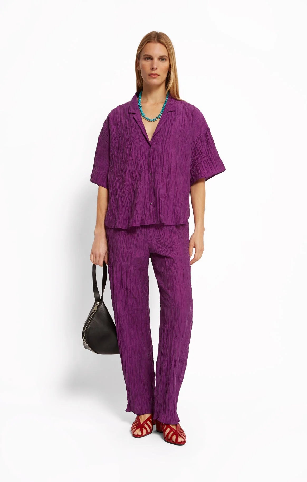 Woman wearing a purple shirt and pants by Roseanna with a plain background