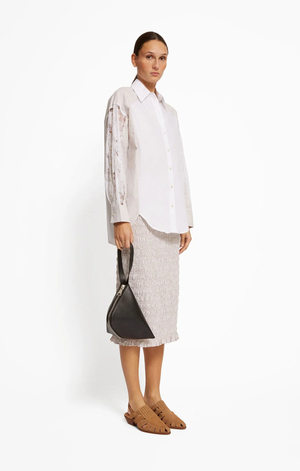 Woman wearing a white shirt and light-colored skirt holding a black handbag on a white background