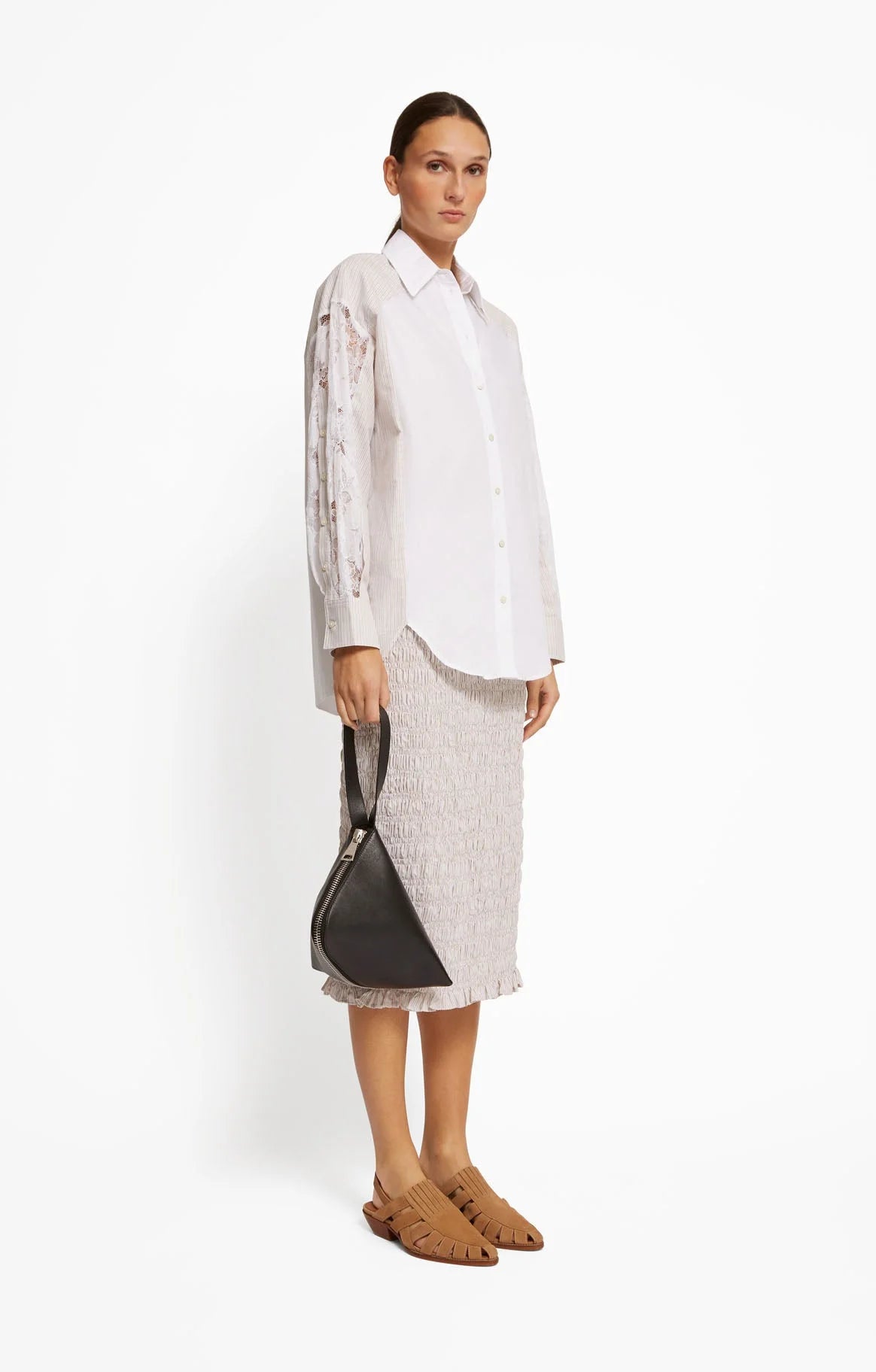Woman wearing a white shirt and light-colored skirt holding a black handbag on a white background