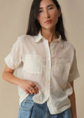 Person wearing a white sheer blouse and blue jeans against a beige background