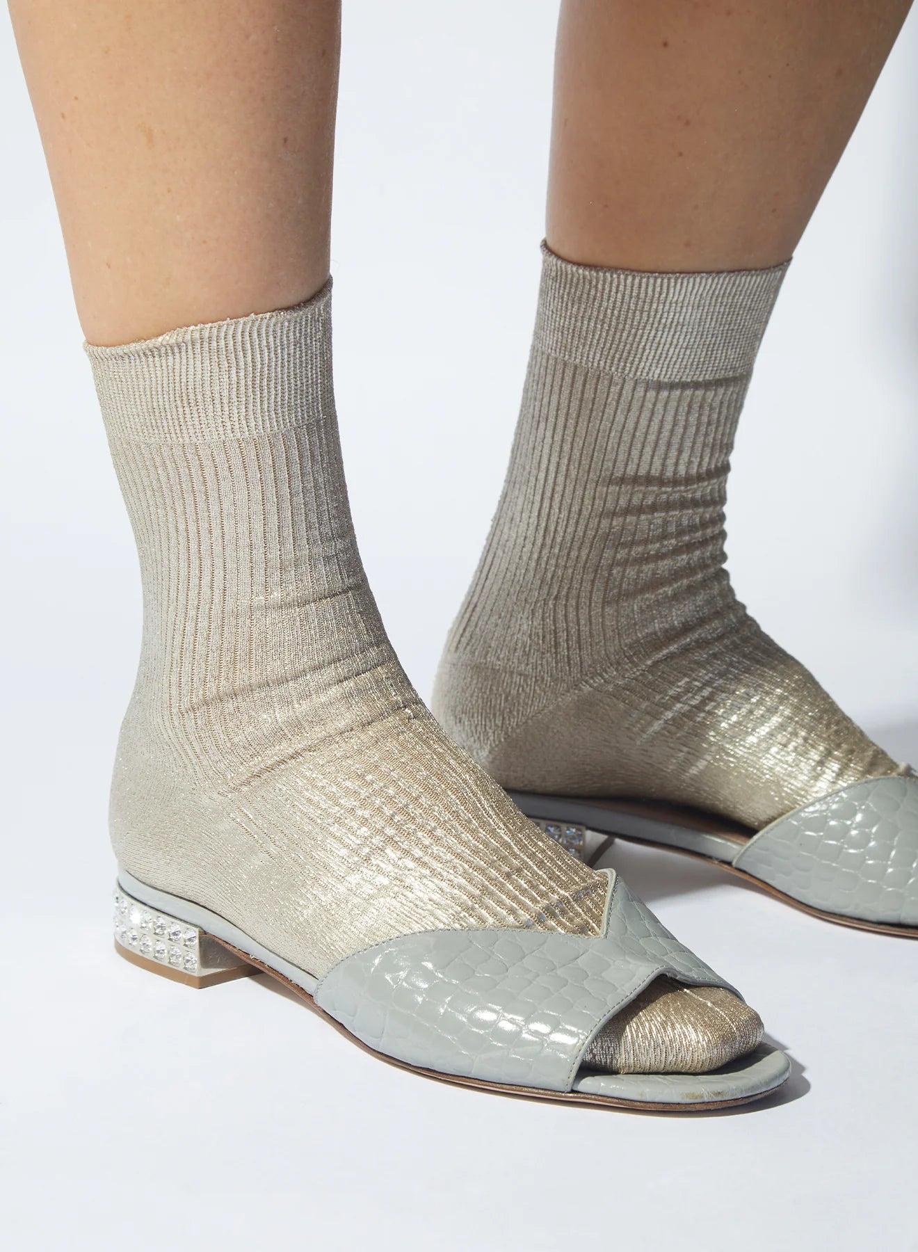 Light gray open-toe shoes with sock-like design worn by a person on a white background