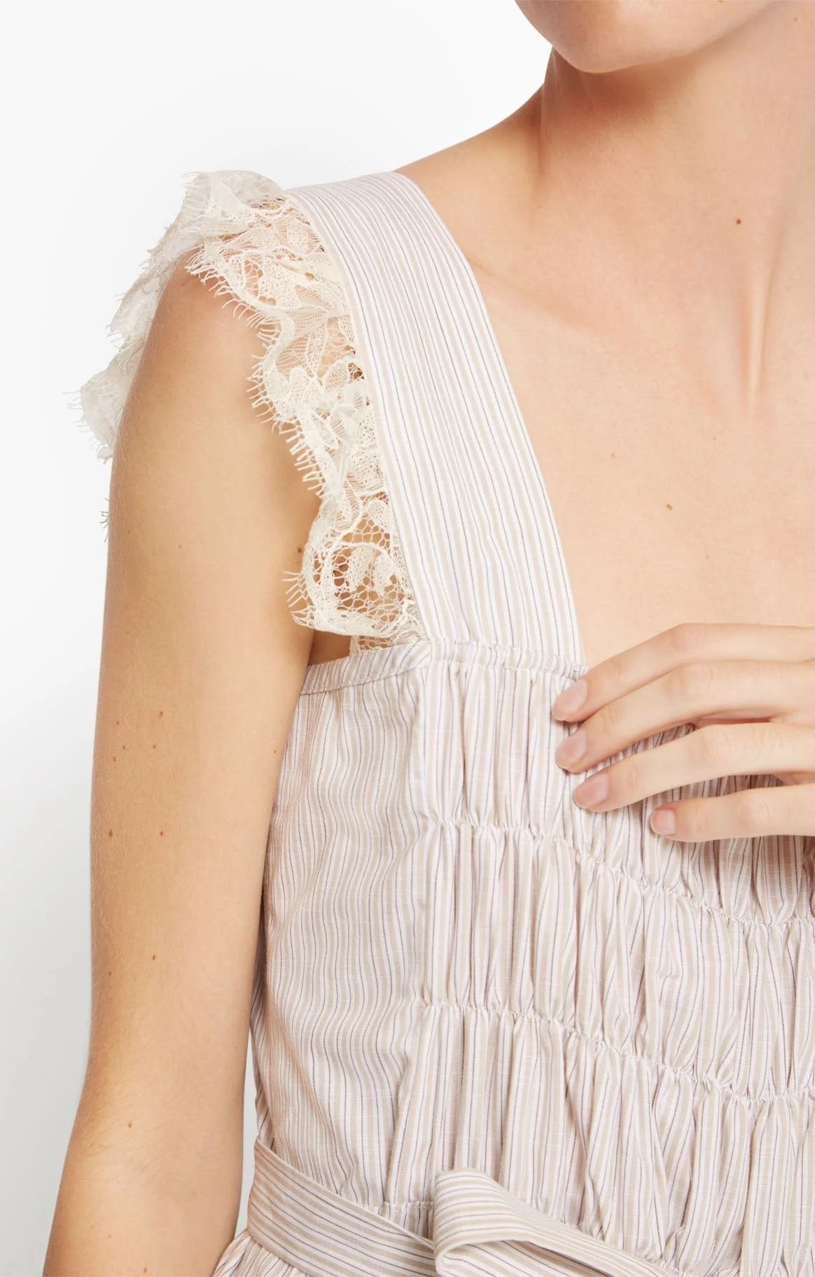 Close-up of a person wearing a beige with white stripes dress with lace details on a white background