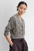 Woman wearing a gray textured cardigan with buttons on a plain background