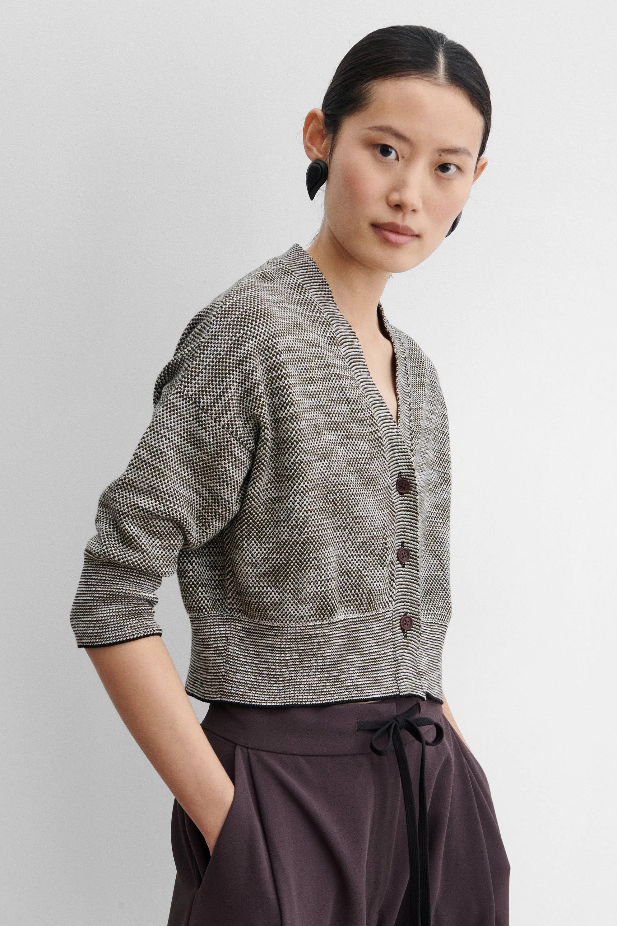 Woman wearing a gray textured cardigan with buttons on a plain background