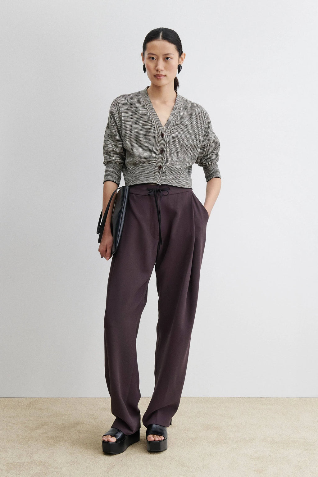Woman wearing a gray cardigan and dark pants against a plain background