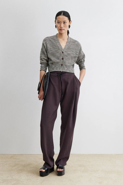 Woman wearing a gray cardigan and dark pants against a plain background