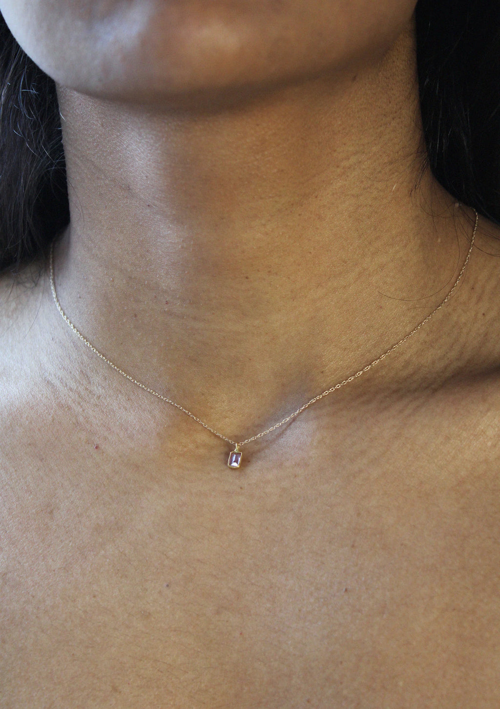 A woman wearing a delicate gold chain necklace with a small rectangular sapphire  pendant by Takara.