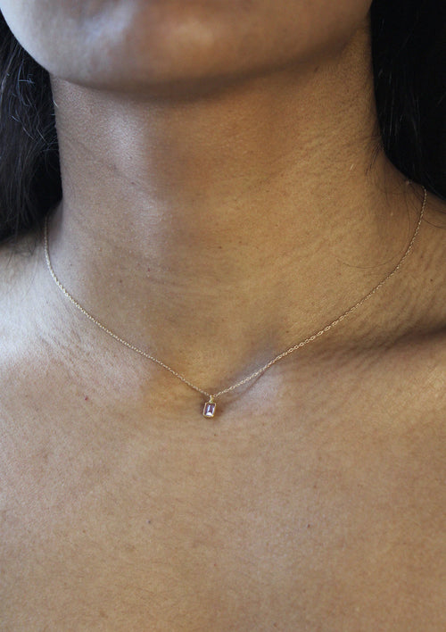 A woman wearing a delicate gold chain necklace with a small rectangular sapphire  pendant by Takara.