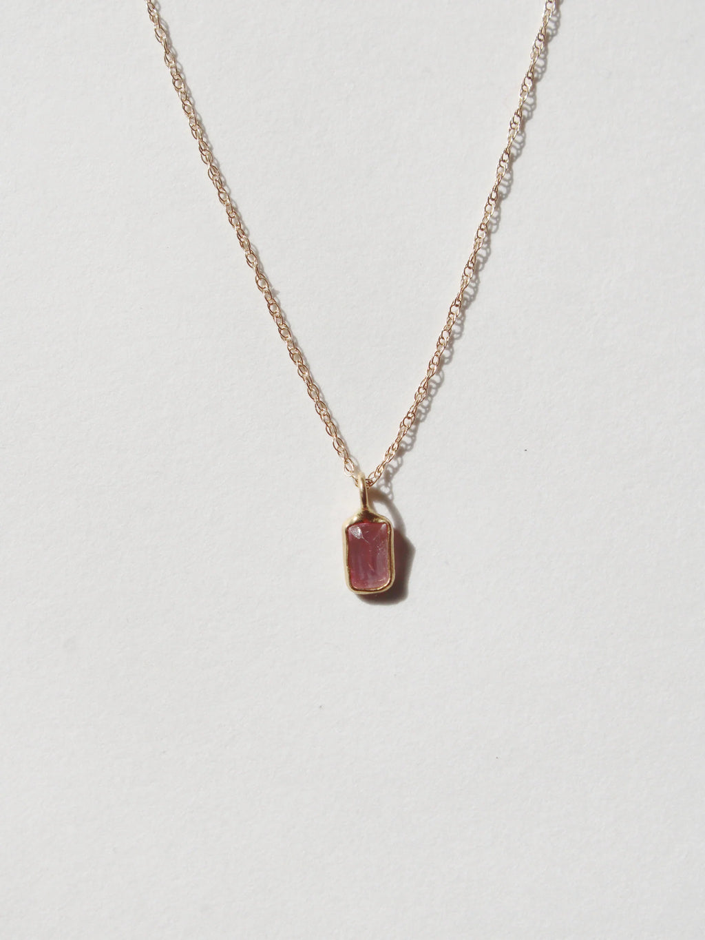 A delicate gold chain necklace with a small rectangular sapphire pendant by Takara.