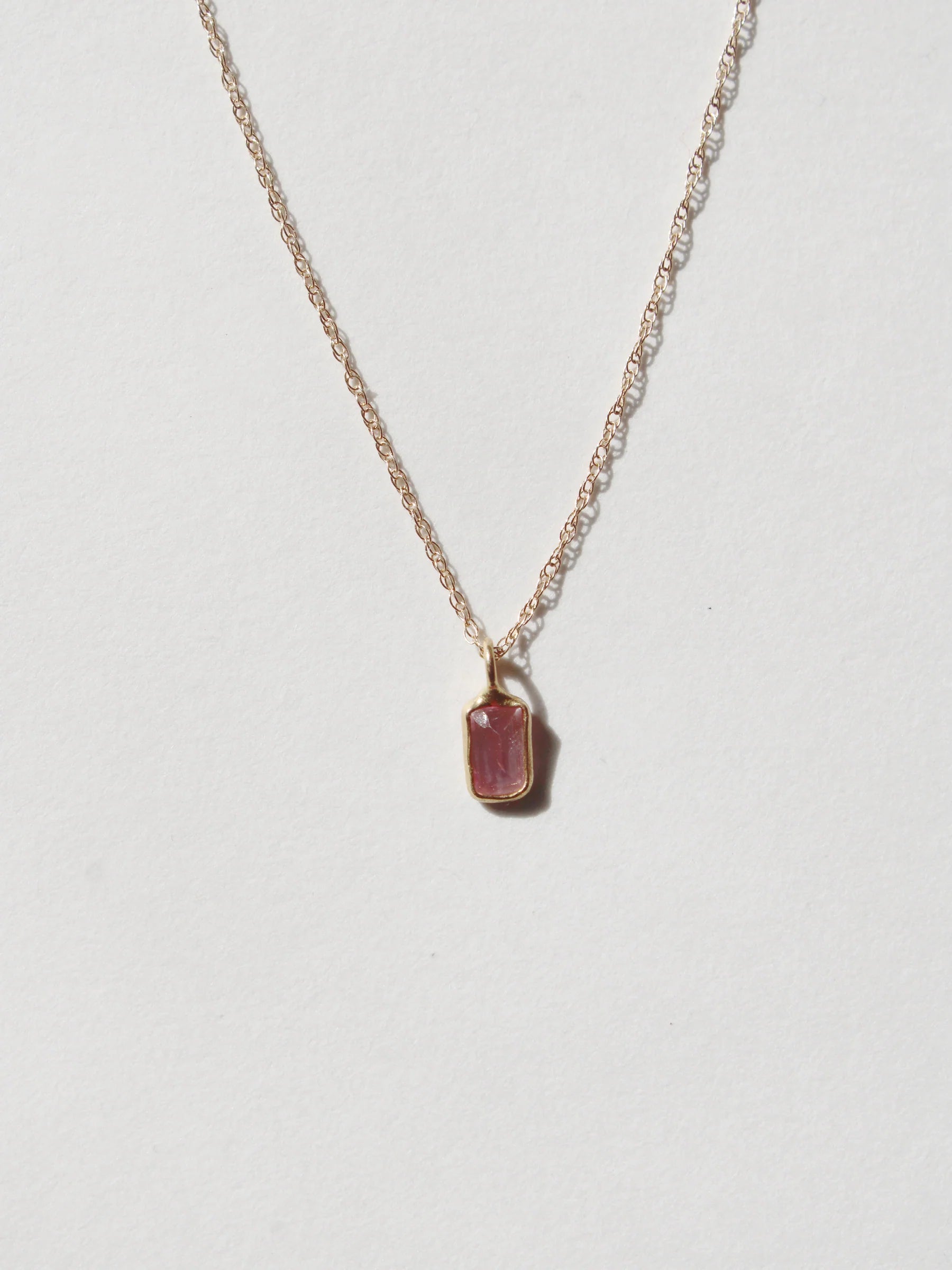 A delicate gold chain necklace with a small rectangular sapphire pendant by Takara.