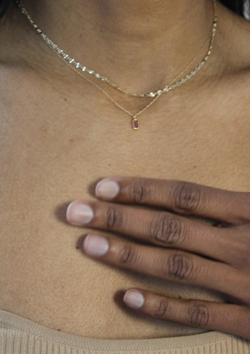 A woman wearing a delicate gold chain necklace with a small rectangular sapphire  pendant by Takara.