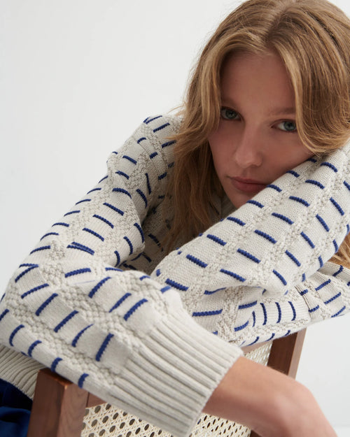 A woman wearing the Thread Jumper Sweater by Kowtow with blue pants on a white background.