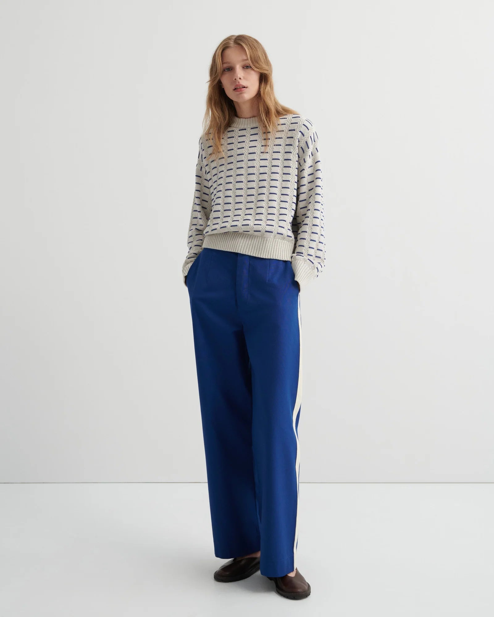 A woman wearing the Thread Jumper Sweater by Kowtow with blue pants on a white background.