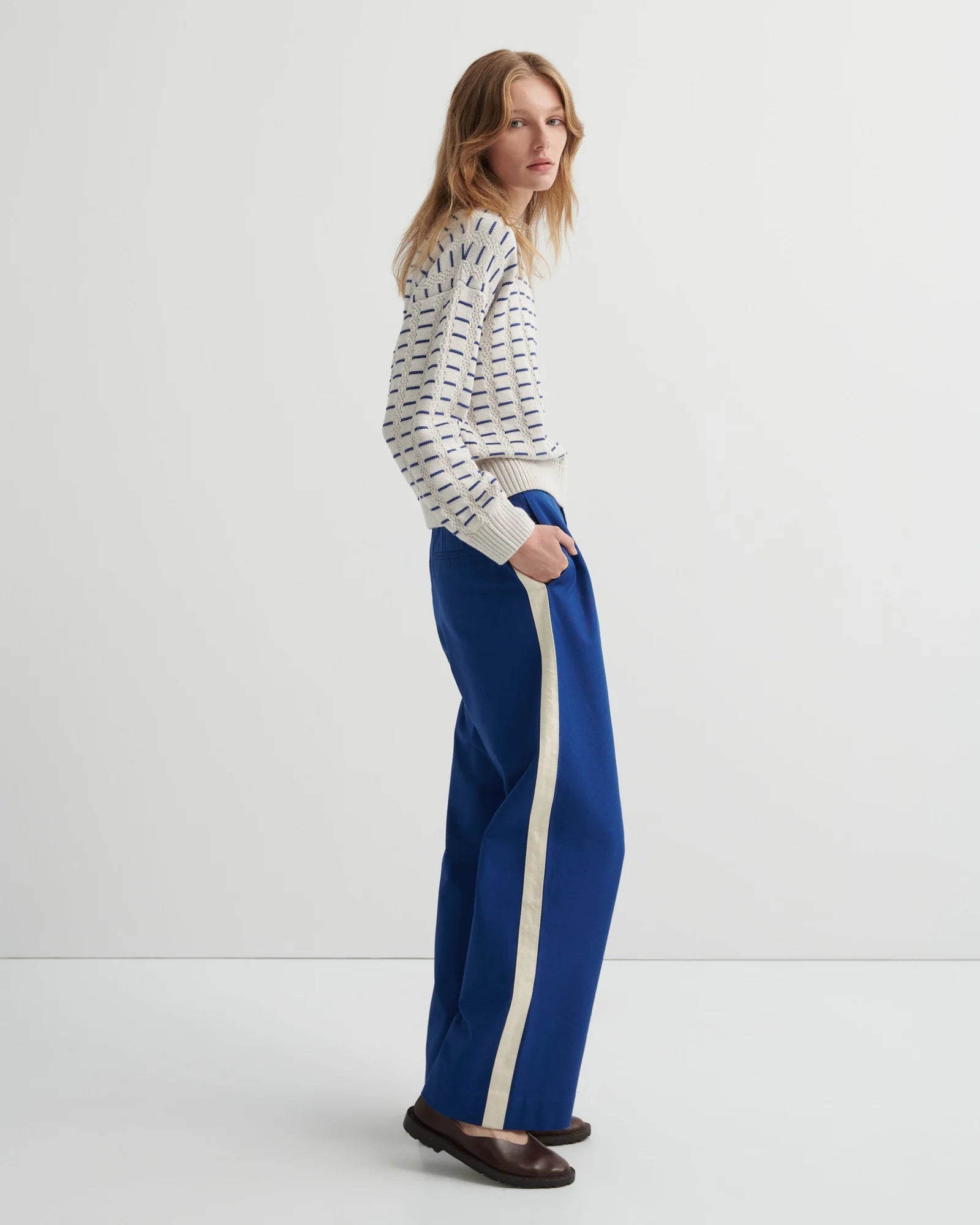 A woman wearing the Thread Jumper Sweater by Kowtow with blue pants on a white background.
