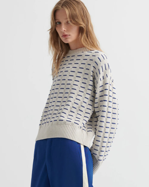 A woman wearing the Thread Jumper Sweater by Kowtow with blue pants on a white background.