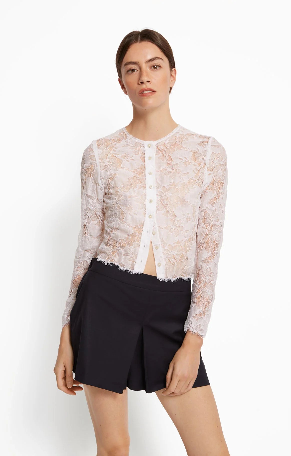 Woman wearing a sheer lace top and black shorts on a white background