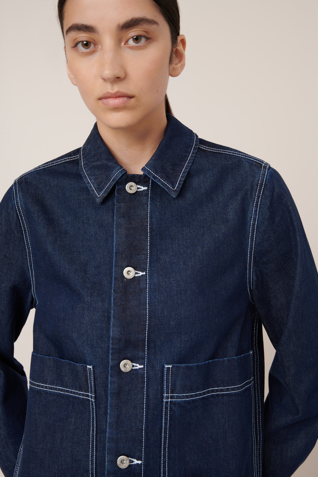 Person wearing a dark blue denim Worker jacket by Kowtow against a plain background